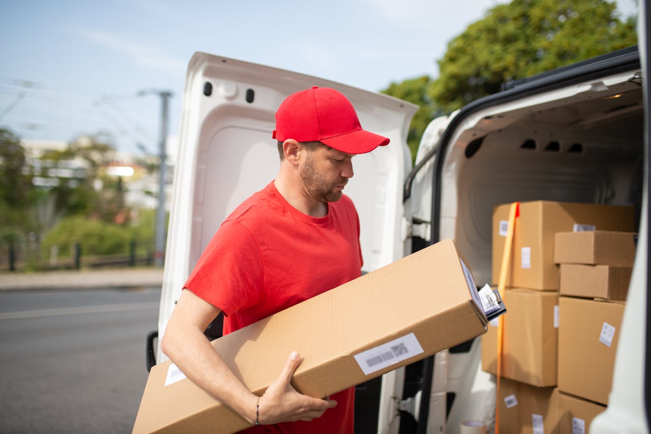 why-choose-us-02 Courier in red uniform unloading packages from a delivery van on a sunny day.